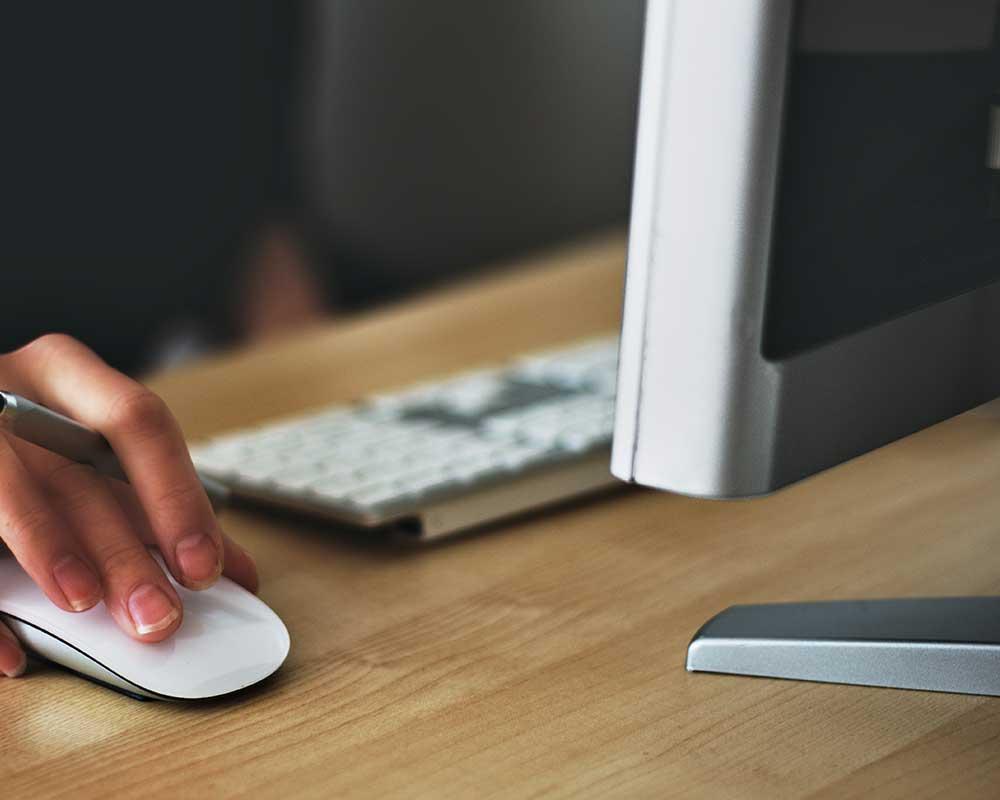 Hand moving computer mouse next to the keyboard and screen